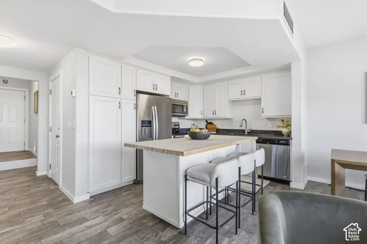 Kitchen featuring white cabinetry, wood-finish flooring, a central island with a wood countertop, and stainless steel appliances