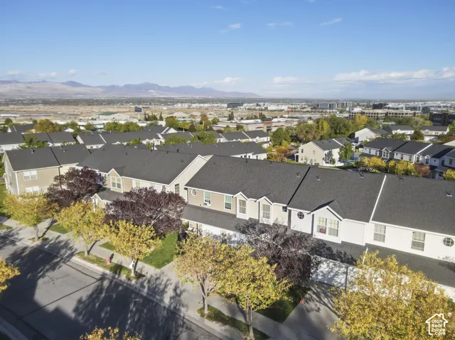 Aerial perspective of a multi-unit residential complex featuring gabled roofs, light-toned siding, mature deciduous trees, and a mountain range backdrop