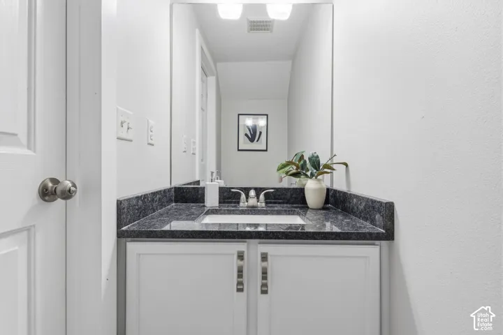 Vanity featuring a dark stone-finish countertop, undermount sink, dual-door white cabinetry, polished metal hardware, and a wall-mounted mirror