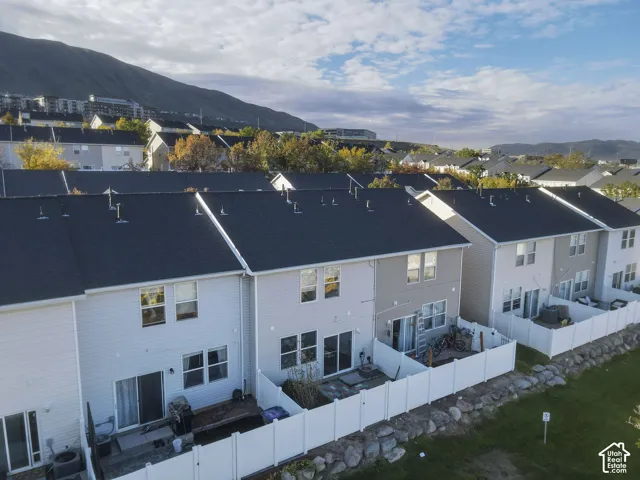 Multi-family residential exterior featuring siding, asphalt shingle roofing, sliding glass patio doors, white vinyl privacy fencing, and mountain backdrop