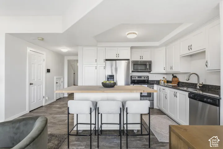 Kitchen featuring white shaker-style cabinetry, dark stone-finish countertops, stainless steel appliances, and a central island with a wood-finish surface