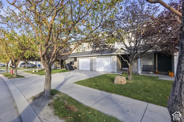 Two-story townhome exterior with vinyl siding, concrete driveway, two-car garage, and mature trees
