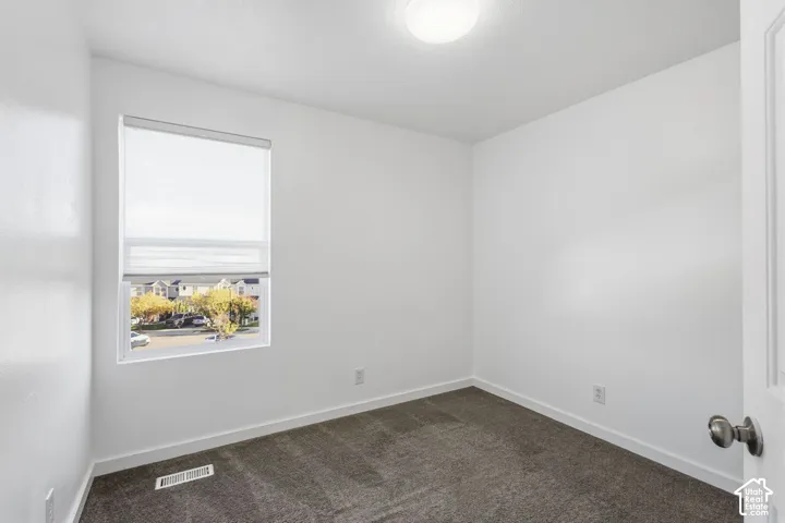 Interior room featuring neutral wall paint, carpeted flooring, a flush-mount ceiling light fixture, and a window with a roller shade