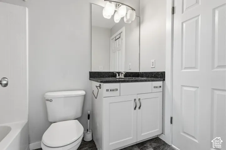 Bathroom featuring a vanity with dark stone countertop, white shaker-style cabinetry, a wall-mounted four-light fixture, and a full-height mirror