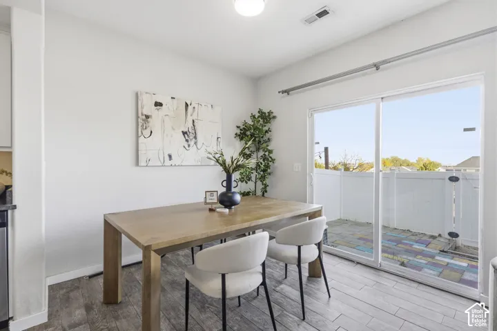 Dining area featuring wood-finish flooring, a flush-mount ceiling light, and sliding glass doors with direct access to a paved patio enclosed by white vinyl fencing