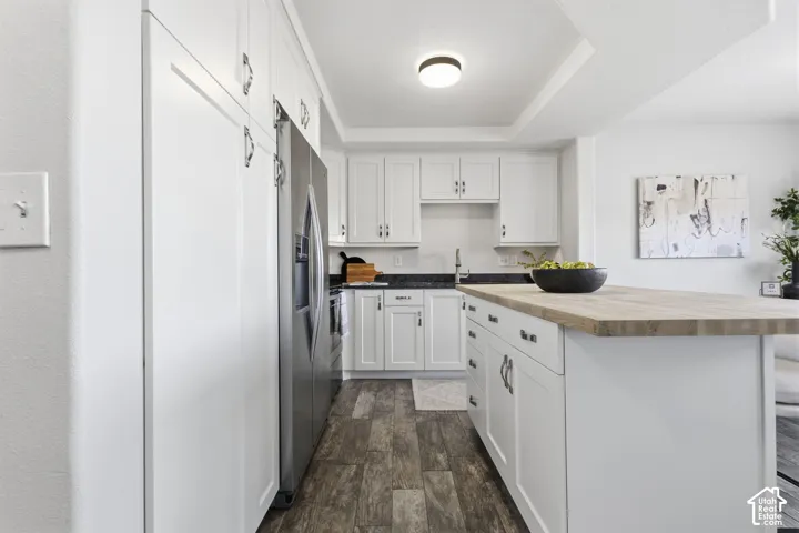 Kitchen featuring white shaker-style cabinetry, stainless steel appliances, a wood-finish countertop island, and dark stone-finish countertops