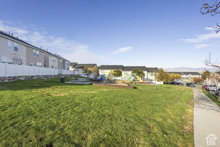 Expansive common area featuring a manicured lawn, paved concrete walkway, integrated playground equipment, and picnic tables
