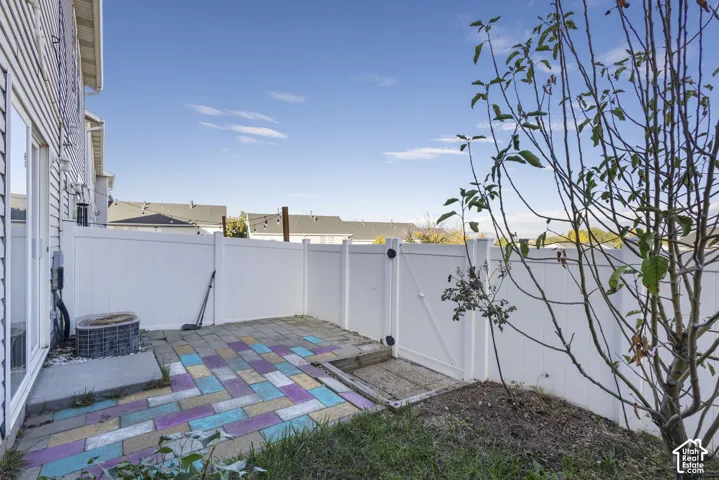Paved patio featuring multicolor interlocking pavers, enclosed by a white vinyl privacy fence with a matching side-access gate