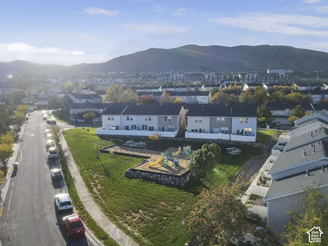 Aerial perspective featuring residential structures, expansive communal lawn, built-in playground equipment, rock retaining walls, and mountain backdrop