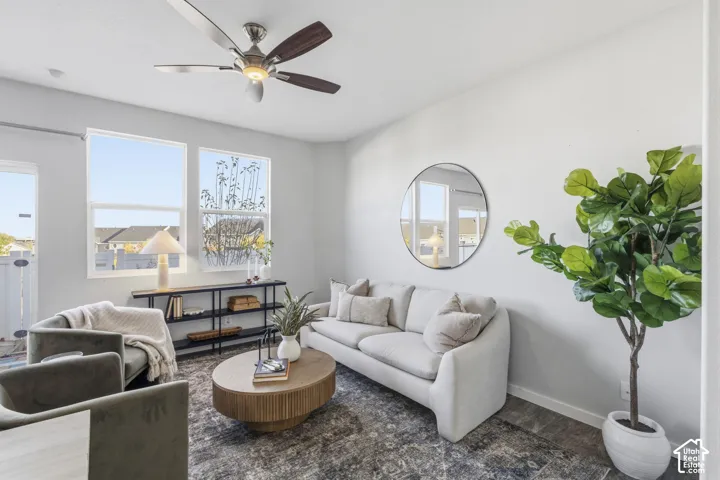 Neutral-toned living space featuring a ceiling fan with integrated lighting, dual windows with exterior exposure, and wood-finish flooring