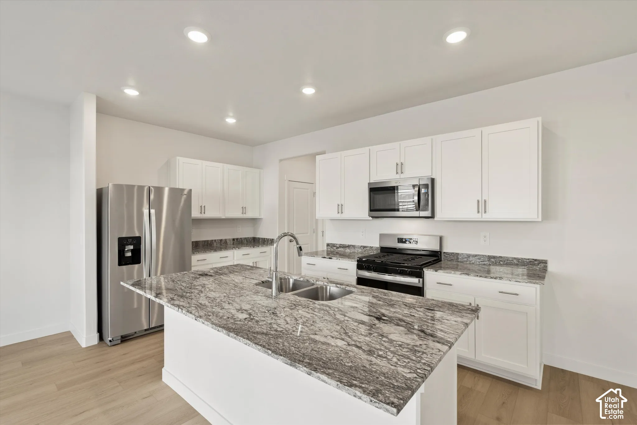 **Disclaimer** Interior package & colors may vary.  Kitchen featuring white cabinetry, stone countertops, a center island with an integrated dual-basin stainless steel sink, stainless steel appliances, and wood-finish flooring