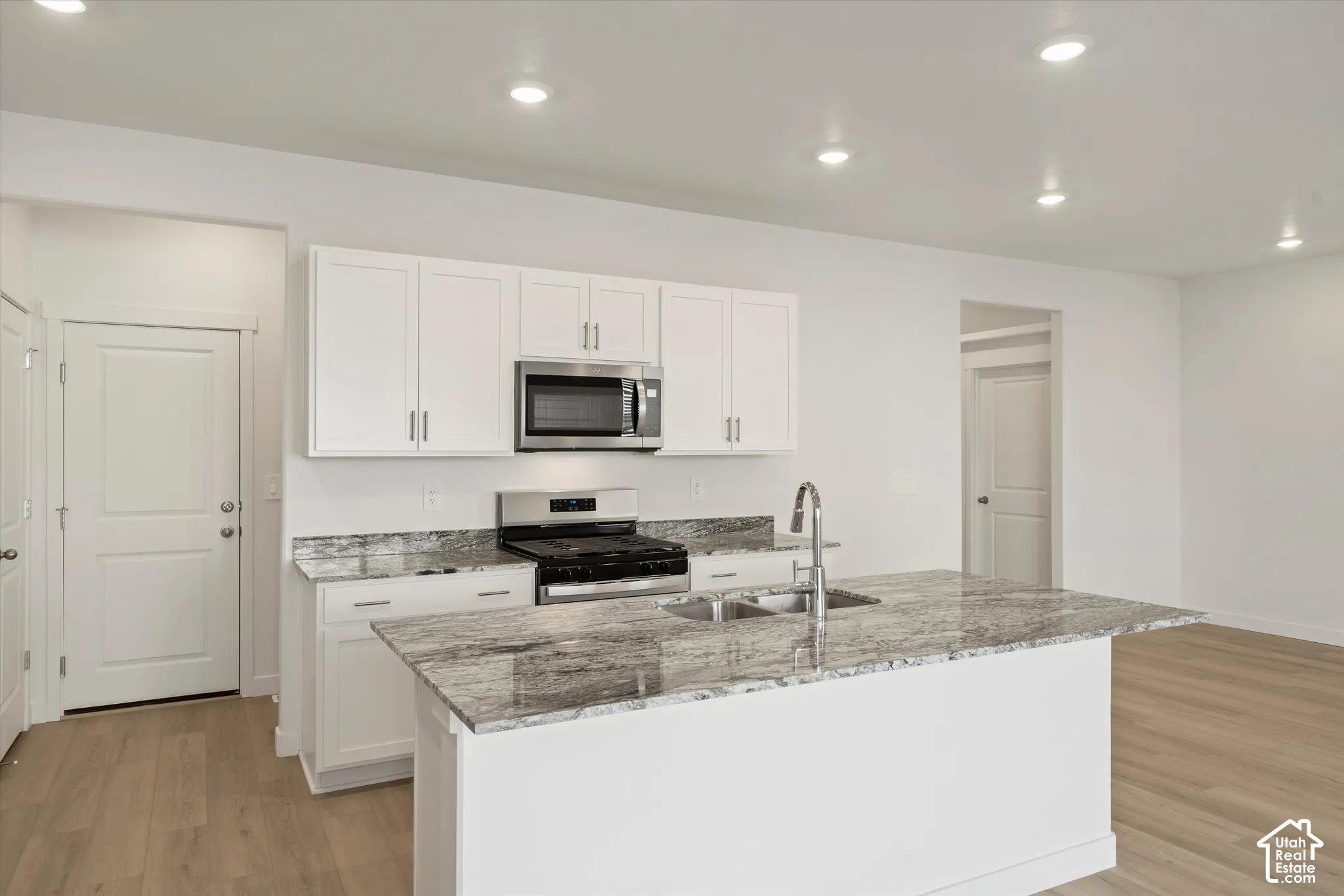 **Disclaimer** Interior package & colors may vary.  Kitchen featuring white shaker-style cabinetry, stone-patterned countertops, a central island, recessed lighting, and wood-finish flooring