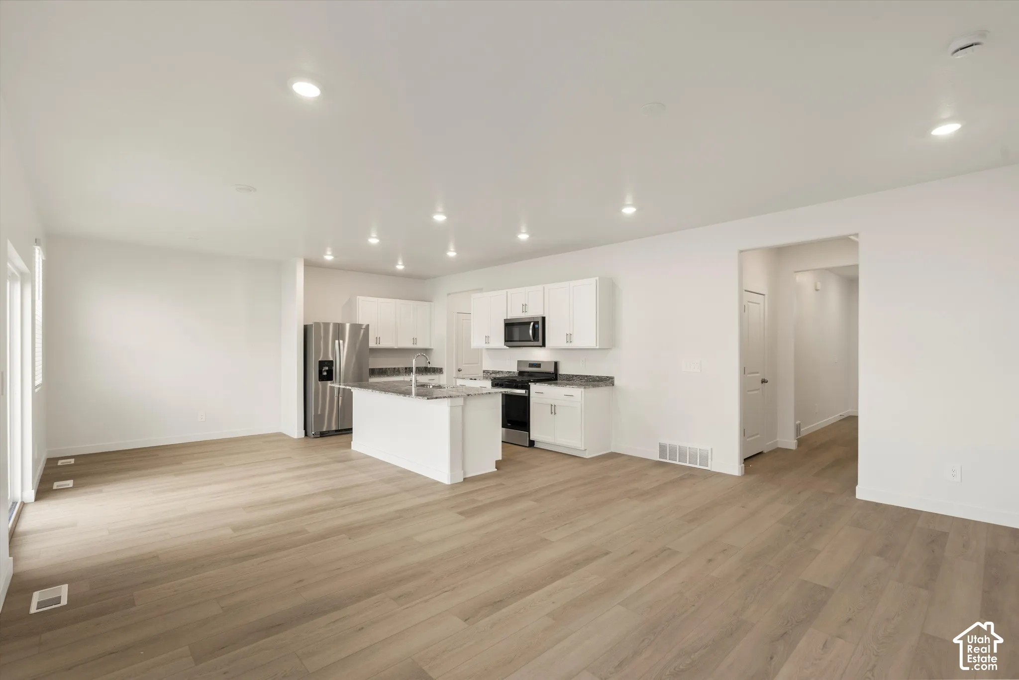 **Disclaimer** Interior package & colors may vary.  Kitchen featuring white cabinetry, stone-finish countertops, stainless steel appliances, a center island with a sink, and wood-finish flooring