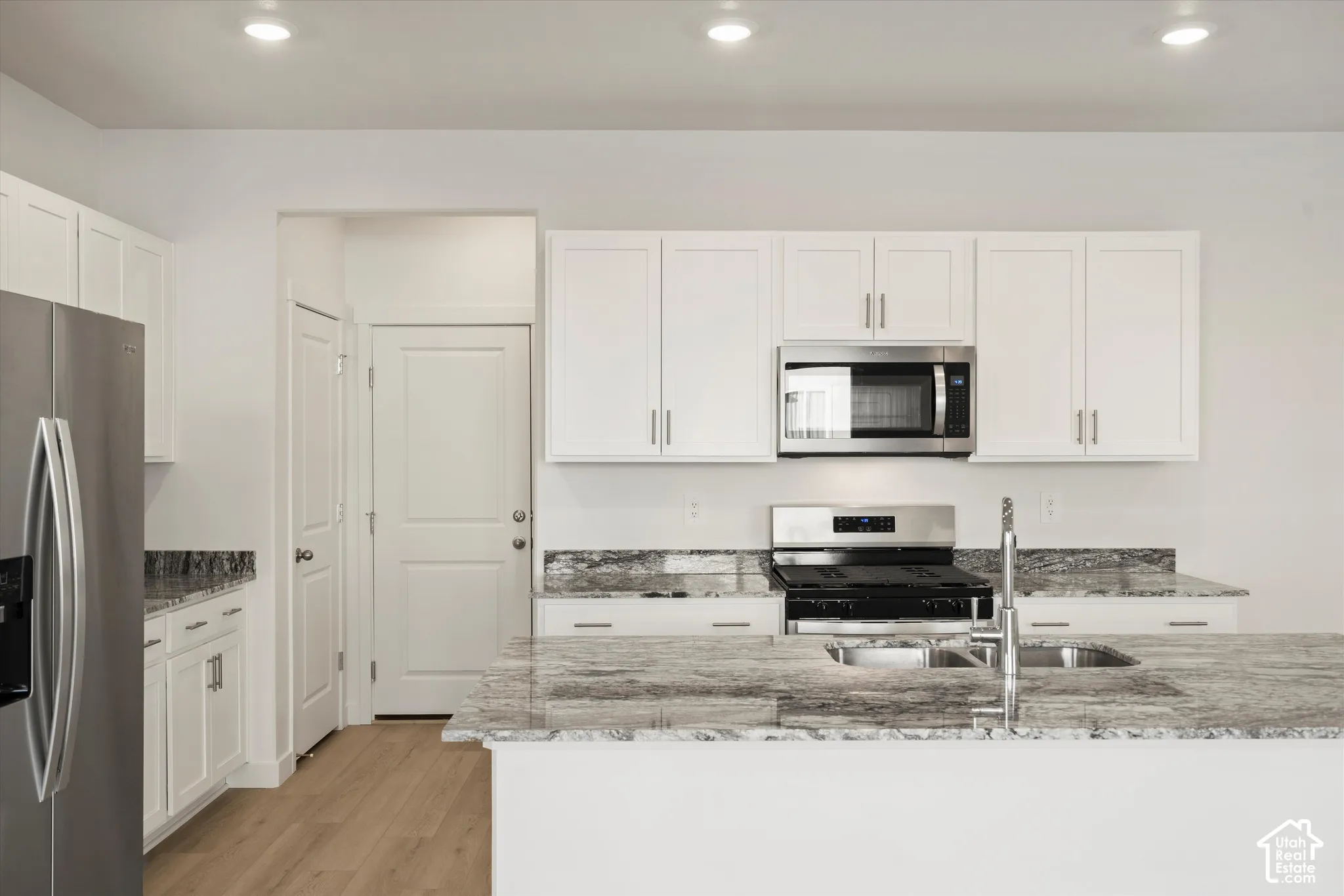 **Disclaimer** Interior package & colors may vary.  Kitchen featuring white shaker-style cabinetry, stone-patterned countertops, a stainless steel refrigerator, a built-in microwave, and wood-finish flooring