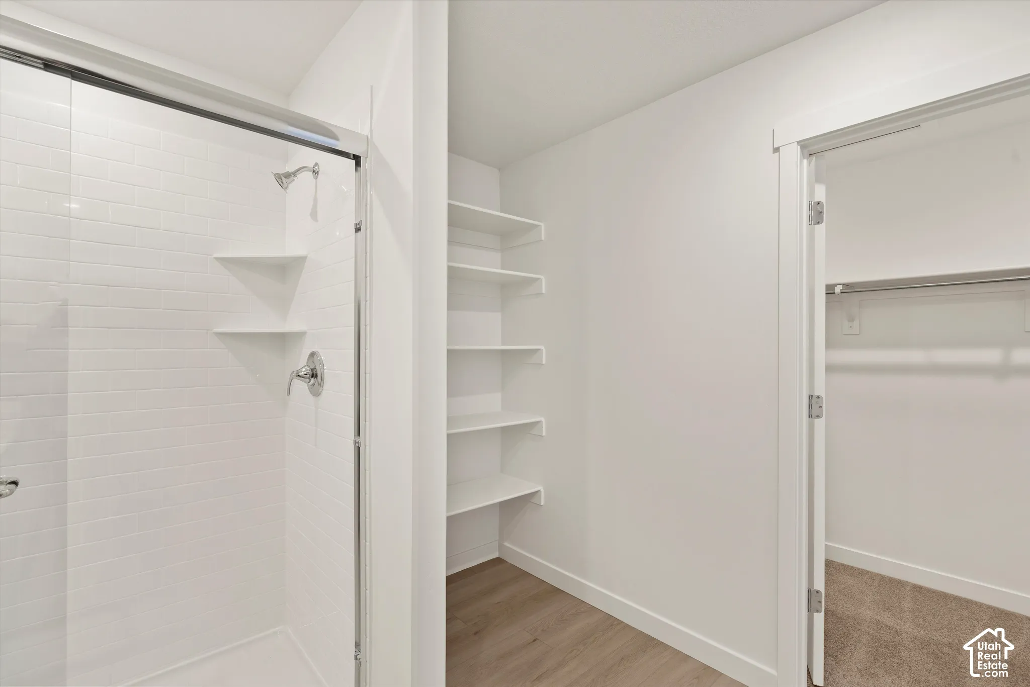 **Disclaimer** Interior package & colors may vary.  Walk-in shower with white subway-style tile, chrome fixtures, and built-in corner shelving, featuring an open-faced storage alcove with tiered shelving and a walk-in closet with carpet flooring and hangi
