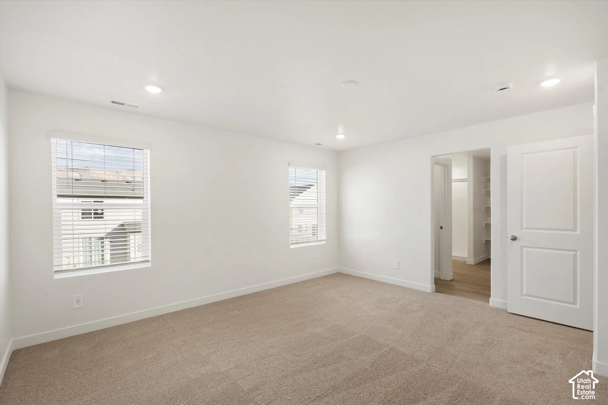 **Disclaimer** Interior package & colors may vary.  Room featuring neutral-toned carpeting, recessed ceiling lighting, two windows with horizontal blinds, and a paneled interior door opening to a walk-in storage area
