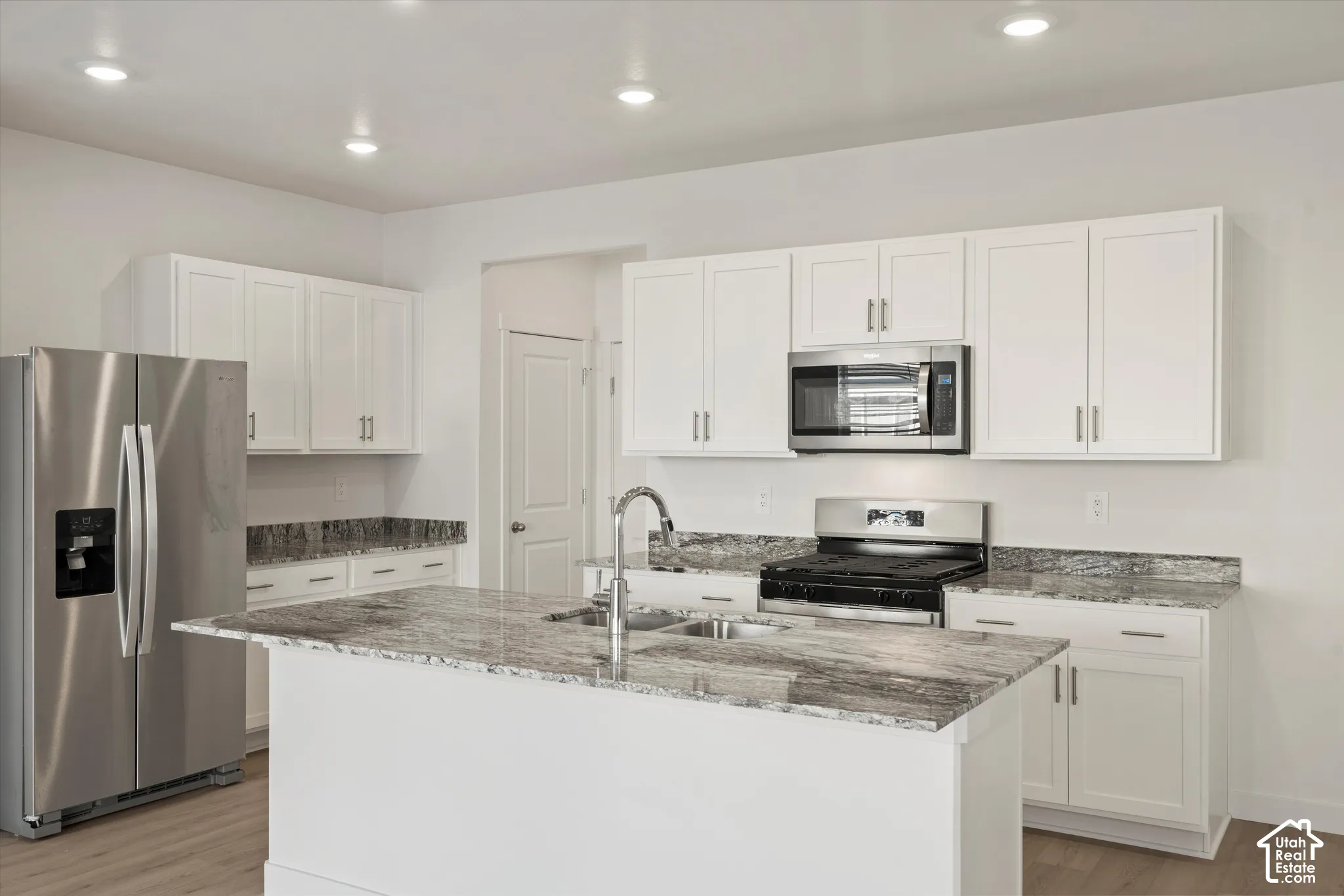 **Disclaimer** Interior package & colors may vary.  Kitchen featuring white shaker-style cabinetry, stone-finish countertops, stainless steel appliances, a center island with a dual-basin sink, and recessed lighting