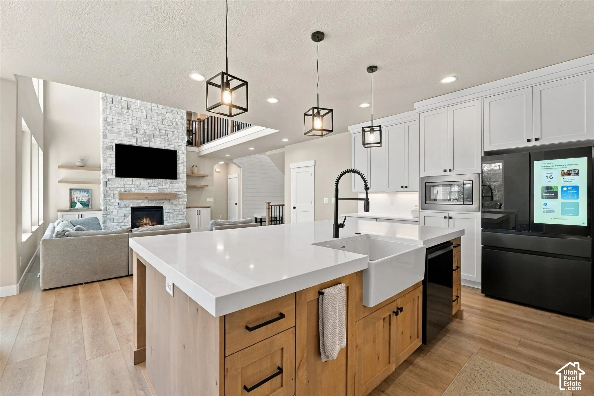Kitchen featuring an expansive island with white countertop, undermount farmhouse sink, matte black gooseneck faucet, and natural-tone wood cabinetry