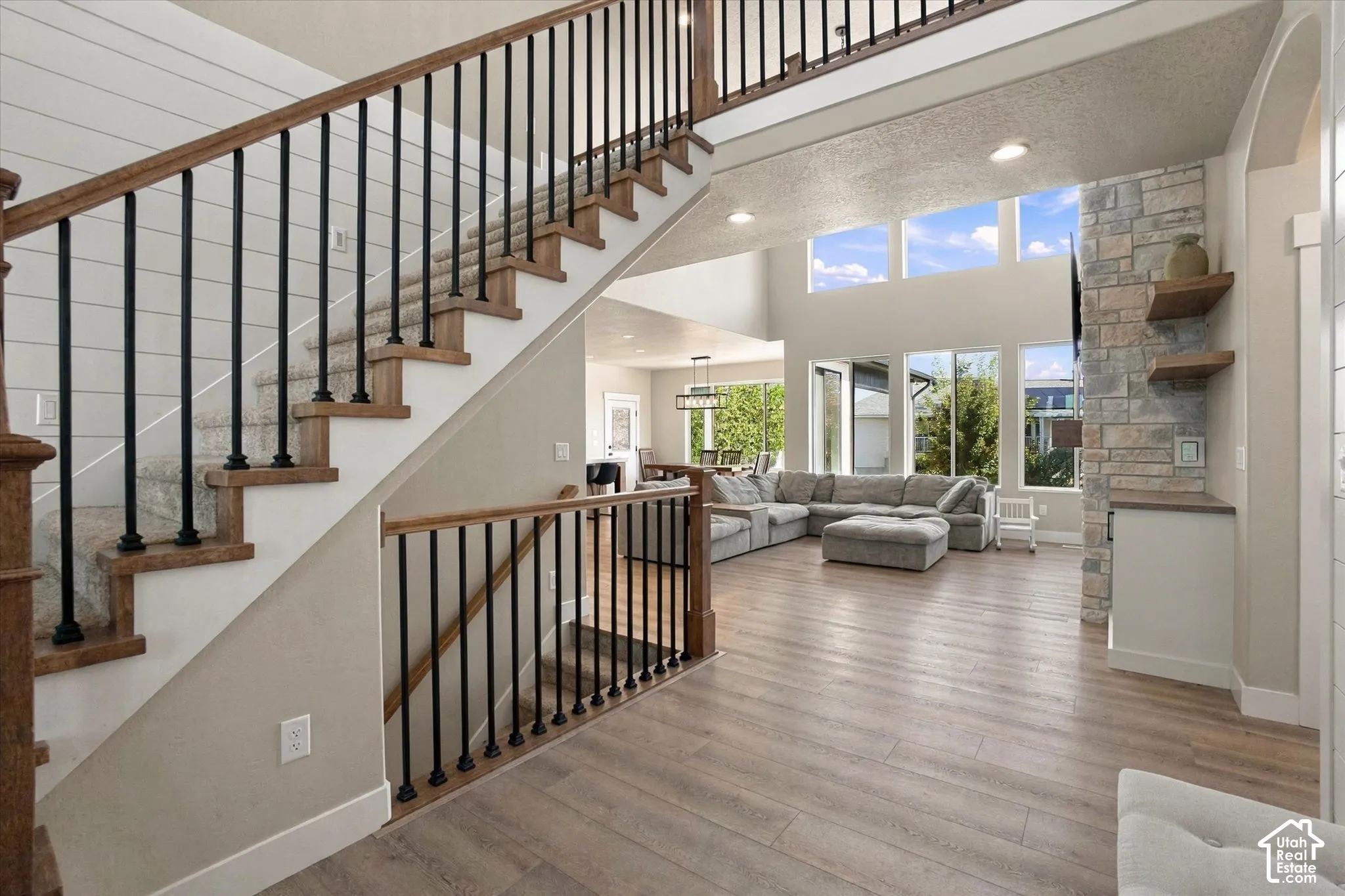 Staircase featuring wood treads and black metal balusters, shiplap wall accent, floor-to-ceiling stone fireplace surround, custom built-in shelving, and wood-finish flooring