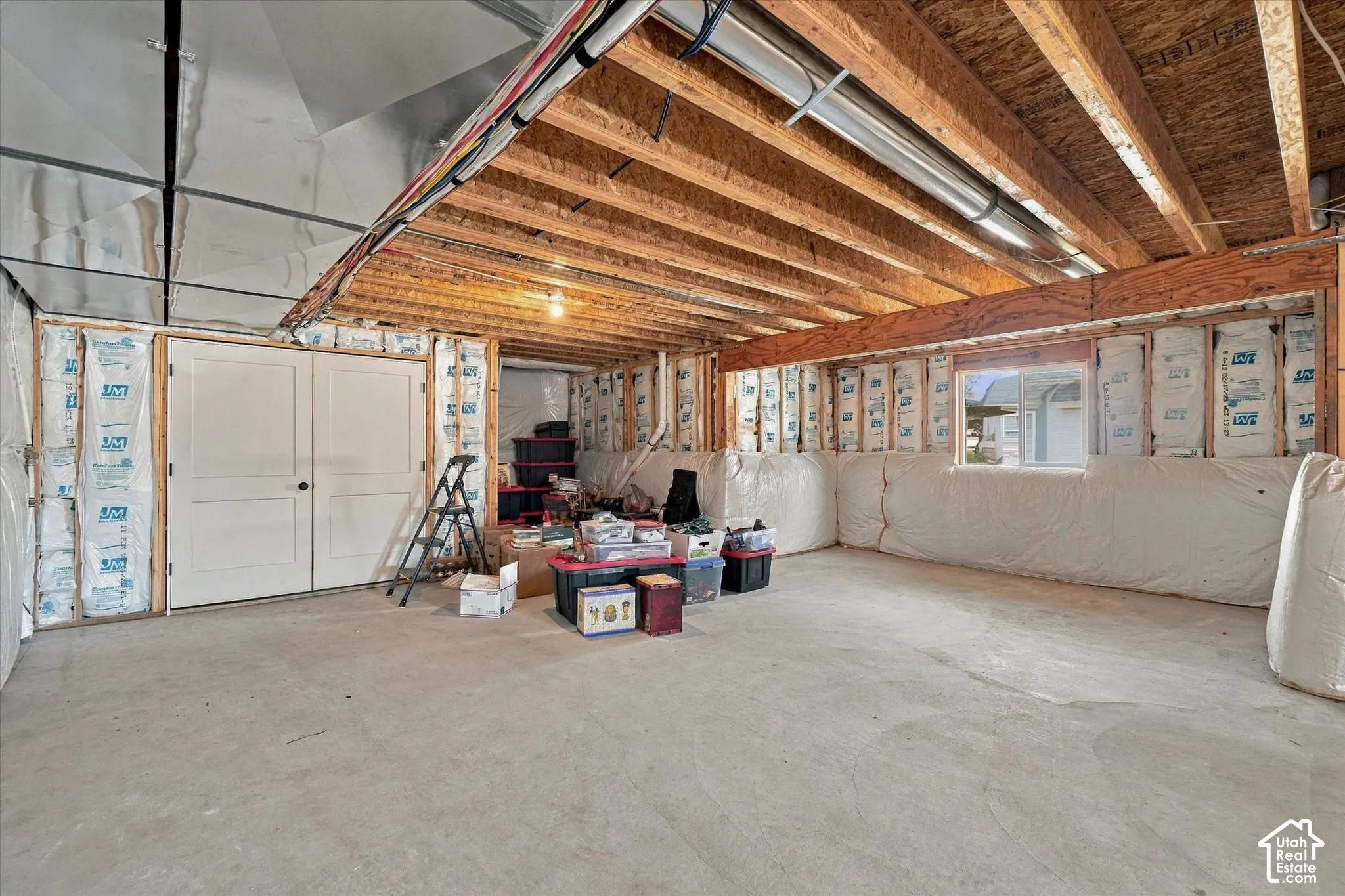 Unfinished lower level featuring exposed wood joist ceilings, concrete flooring, insulated wall paneling, and a double-door entry