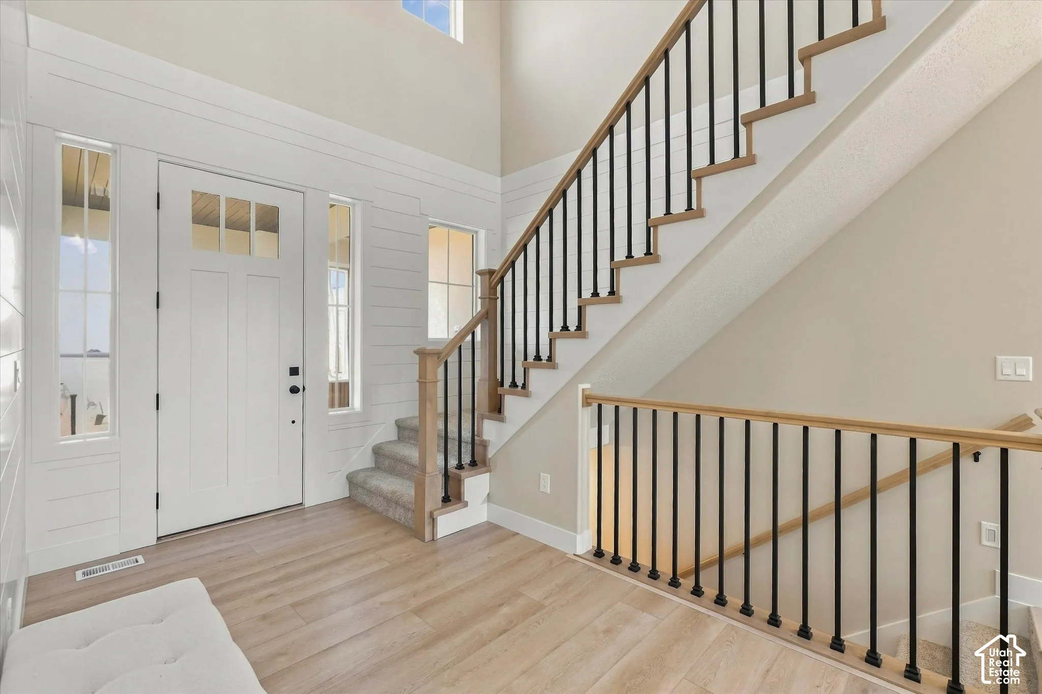 Double-height entryway featuring shiplap wall paneling, wood-finish flooring, a staircase with matte black metal balusters, and a solid door with sidelight windows