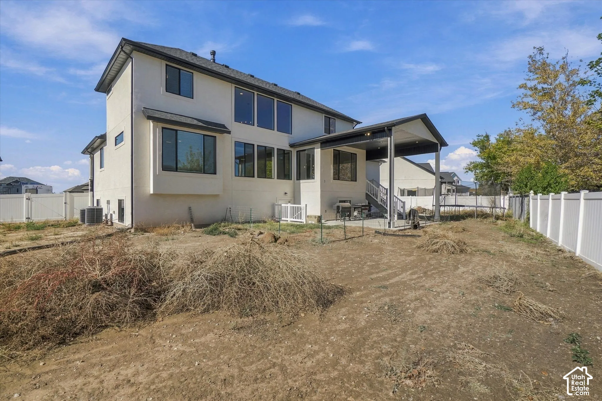 Two-story stucco exterior featuring a covered patio, multiple large picture windows, and a fully fenced perimeter