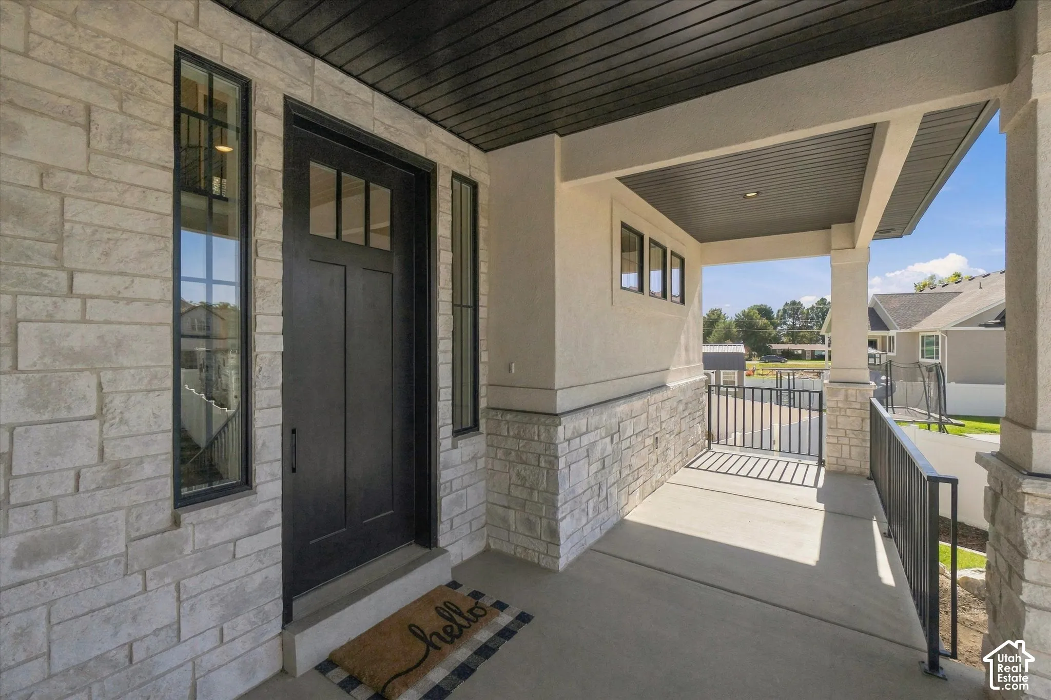 Covered entryway featuring stacked stone veneer, a solid door with transom glass, dark-finished horizontal tongue-and-groove ceiling, and metal railing