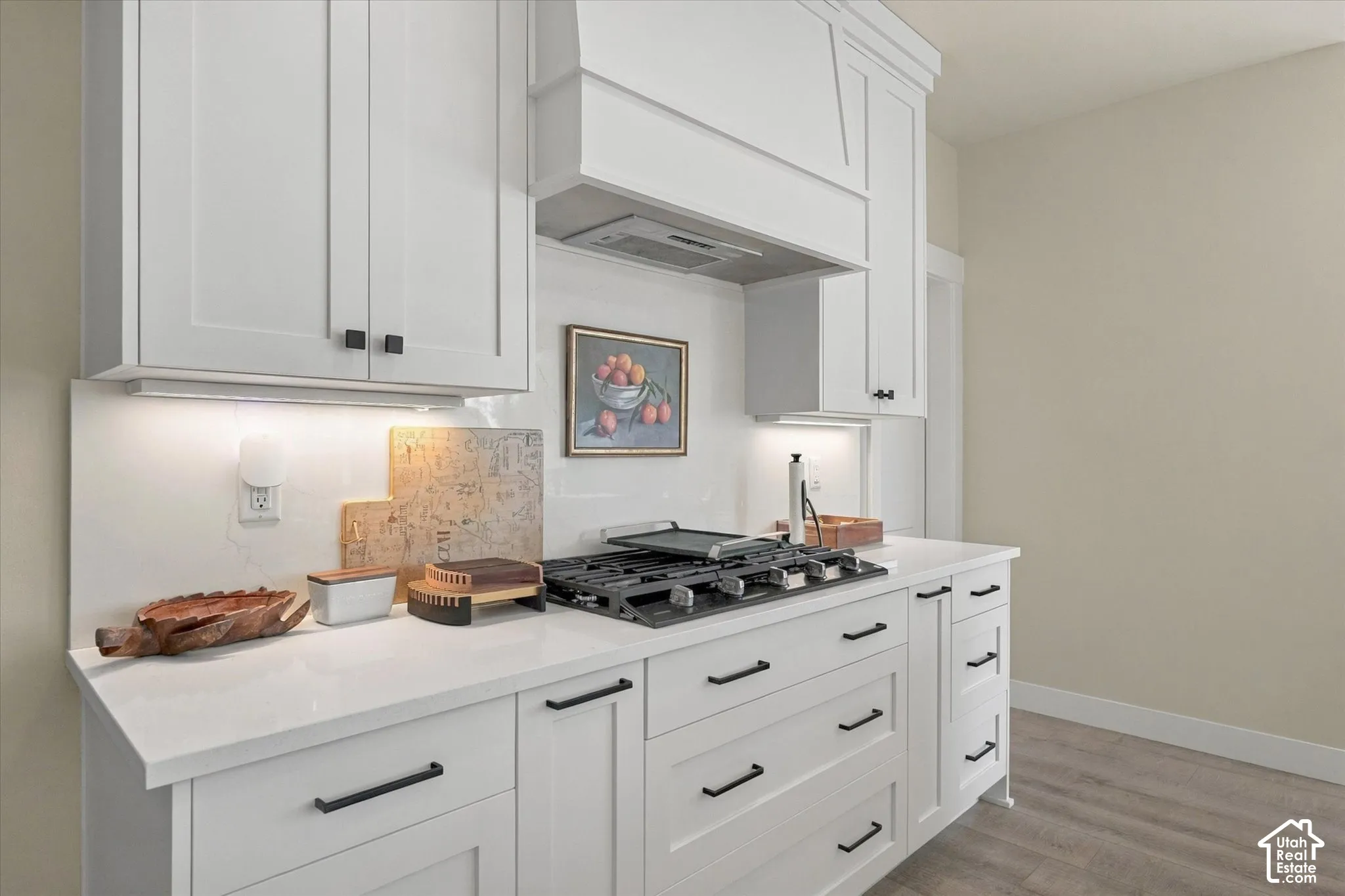 Shaker-style cabinetry with matte black hardware, stone-composite countertops, full-height backsplash, custom range hood enclosure, and gas cooktop