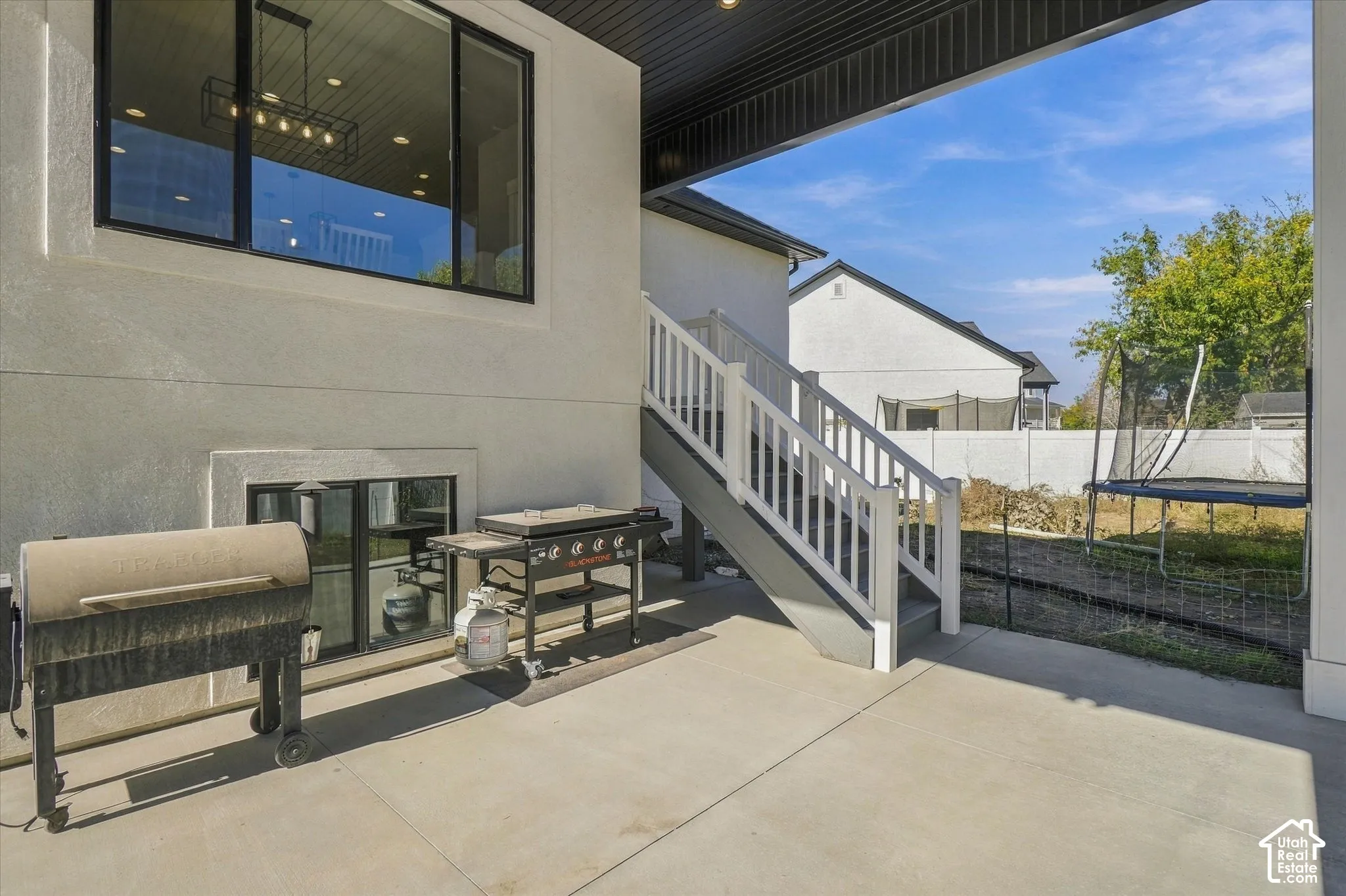 Covered concrete patio featuring a large window, recessed lighting, and a staircase with white railings