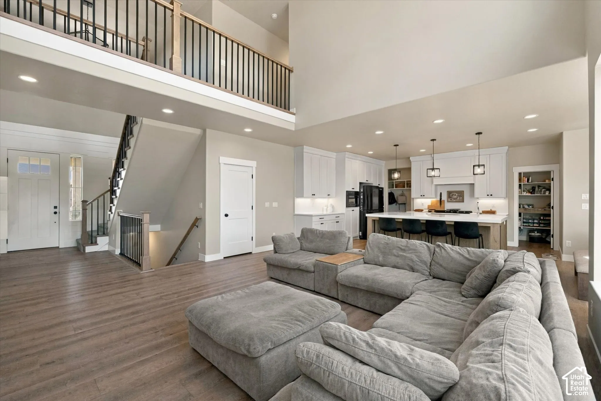 Open-concept interior featuring wood-finish flooring, soaring vaulted ceilings, a kitchen with white cabinetry and a center island, and an elevated mezzanine with a metal spindle railing
