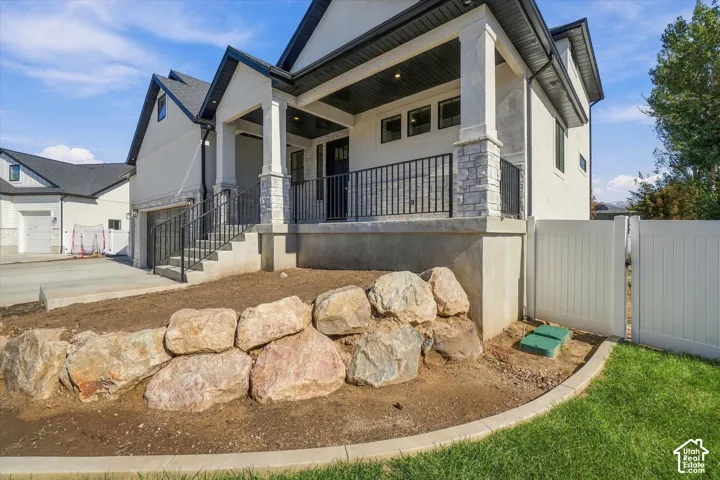 Exterior featuring a multi-gable roofline, stacked stone and stucco siding, a covered front porch with metal railings, and a boulder retaining wall