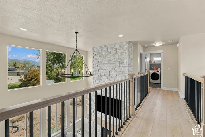 Elevated landing featuring wood-finish flooring, metal spindle railing, floor-to-ceiling stone-faced chimney, modern multi-arm chandelier, and recessed lighting