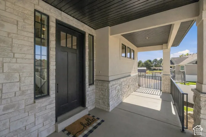 Covered entryway featuring stacked stone veneer, a solid door with transom glass, dark-finished horizontal tongue-and-groove ceiling, and metal railing