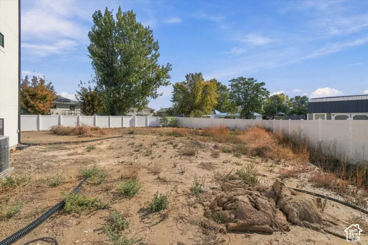 Rear exterior yard featuring a perimeter vinyl fence and mature trees