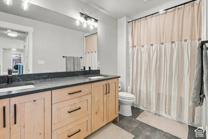 Double vanity featuring light wood-finish cabinetry, dark contrasting countertops with integrated sinks, matte black hardware, and an expansive wall-mounted mirror