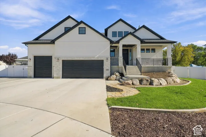 Multi-gabled exterior featuring light-toned smooth siding, stone veneer accents, an expansive concrete driveway, a three-car garage, and a covered porch with metal railings