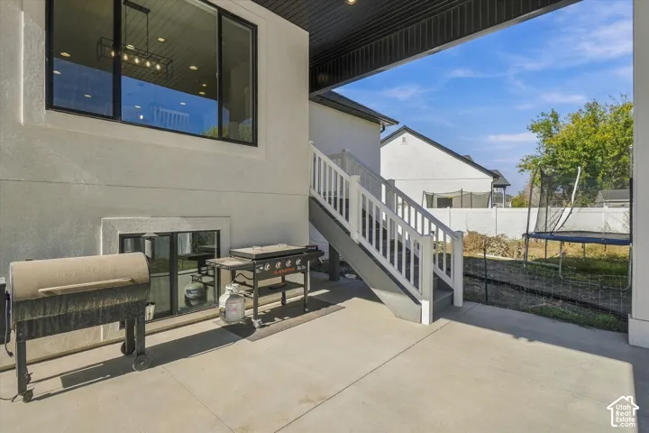 Covered concrete patio featuring a large window, recessed lighting, and a staircase with white railings