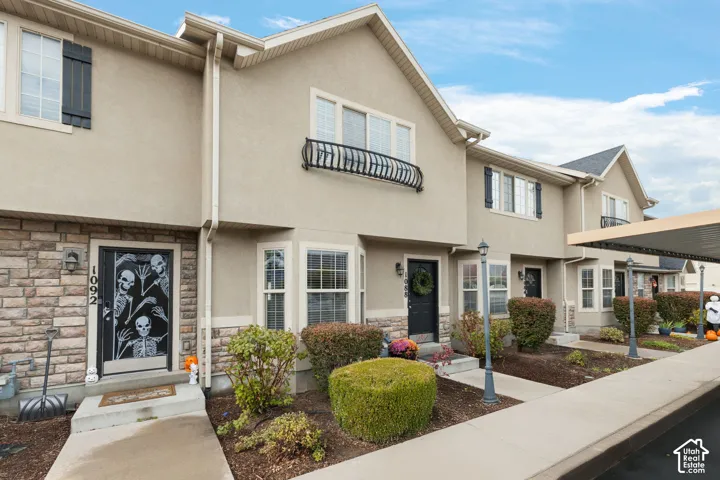 Multi-level townhome exterior featuring a stucco facade, stone veneer accents, decorative metal railings, and attached covered parking