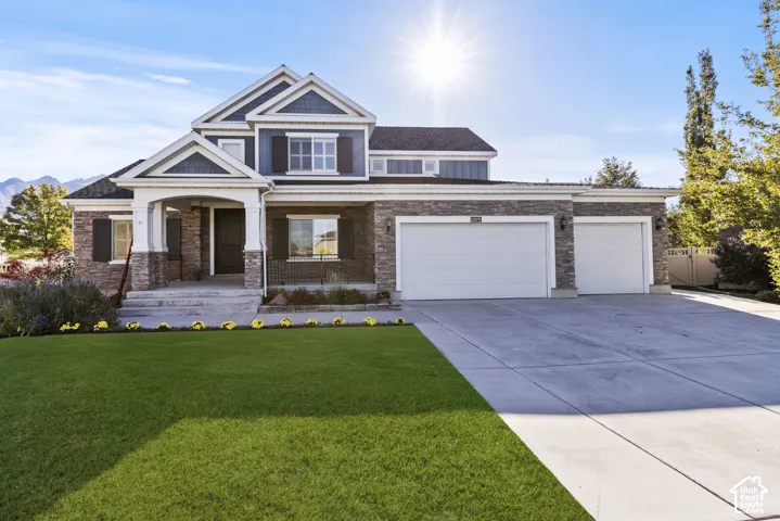 Multi-level residence featuring a stone and siding exterior, covered front porch with columns, and an attached three-car garage