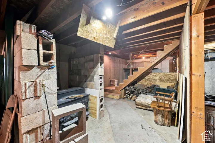 Unfinished basement featuring exposed wood ceiling joists, concrete masonry unit walls, open wooden staircase, and concrete floor