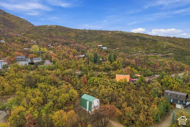 Aerial perspective of a multi-level structure featuring a green metal roof and light-toned siding, situated within a dense forest of deciduous trees on a hillside