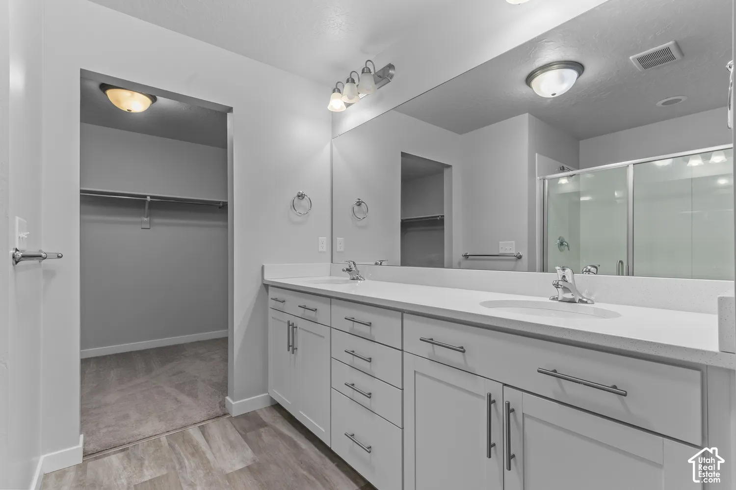 Dual-sink vanity with white cabinetry, light-toned countertop, large wall-spanning mirror, and shower enclosure with glass doors