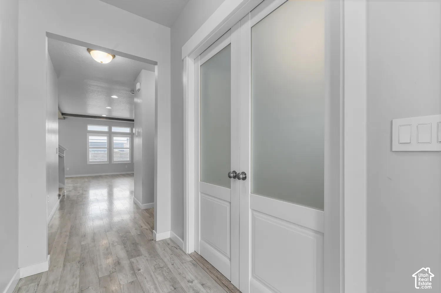 White double doors with frosted glass panels, neutral wall palette, and wood-finish flooring