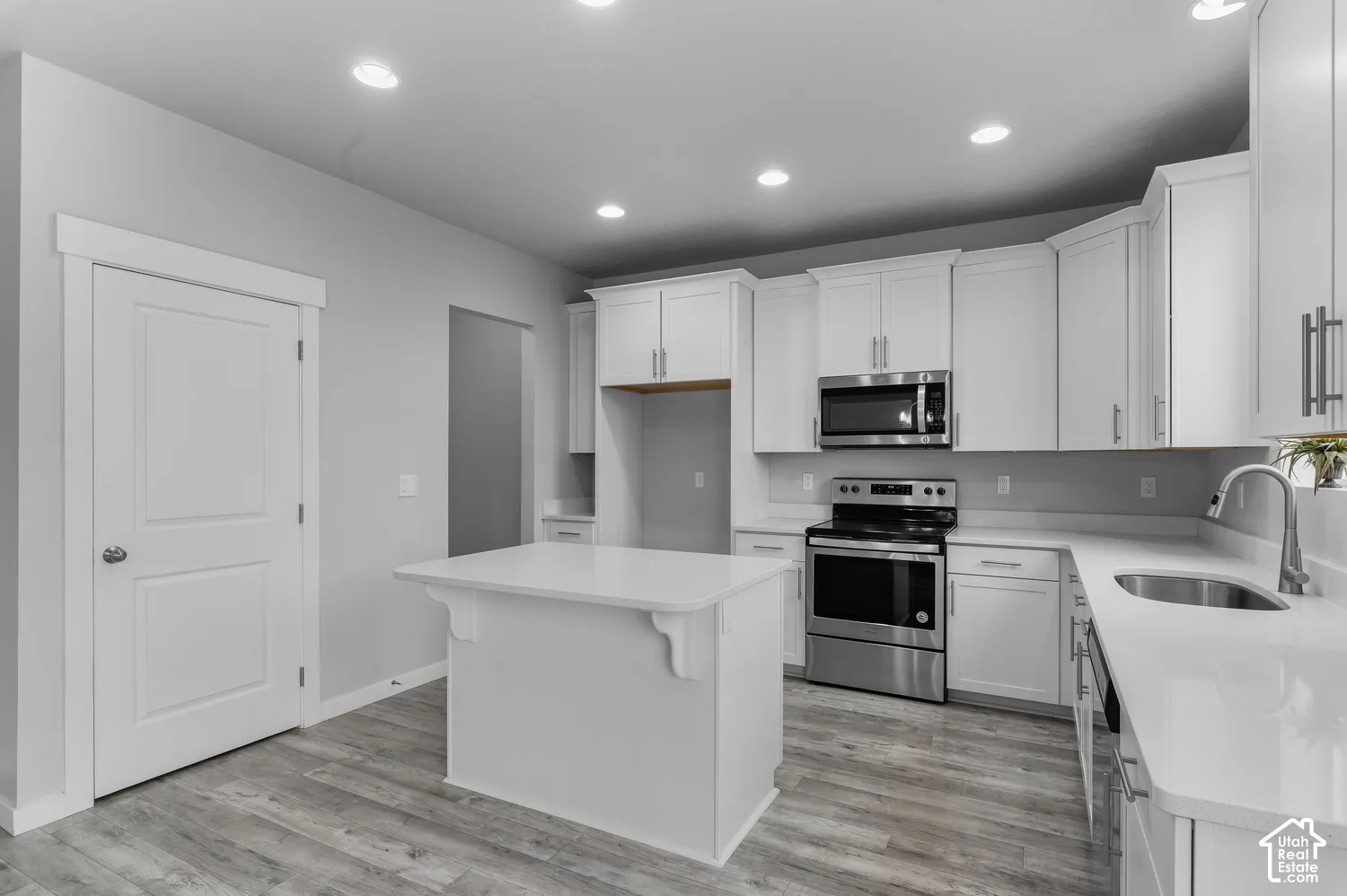 Kitchen featuring white cabinetry, an island with a quartz countertop, stainless steel appliances, and wood-finish flooring