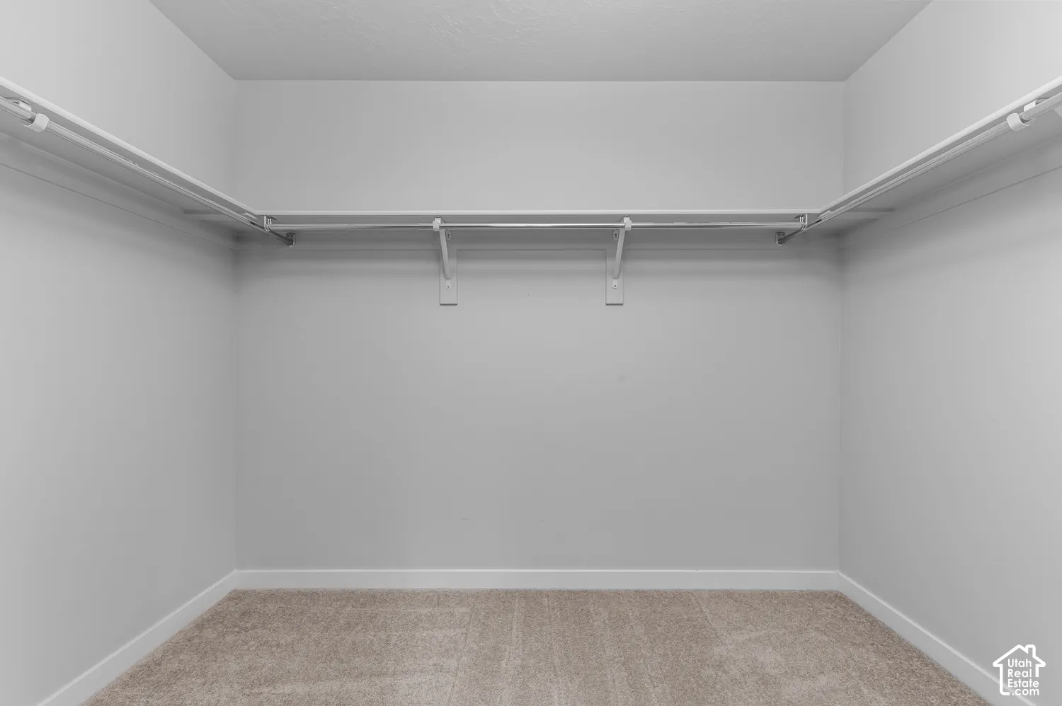 Walk-in closet featuring neutral carpeting and wrap-around built-in shelving with integrated hanging rods