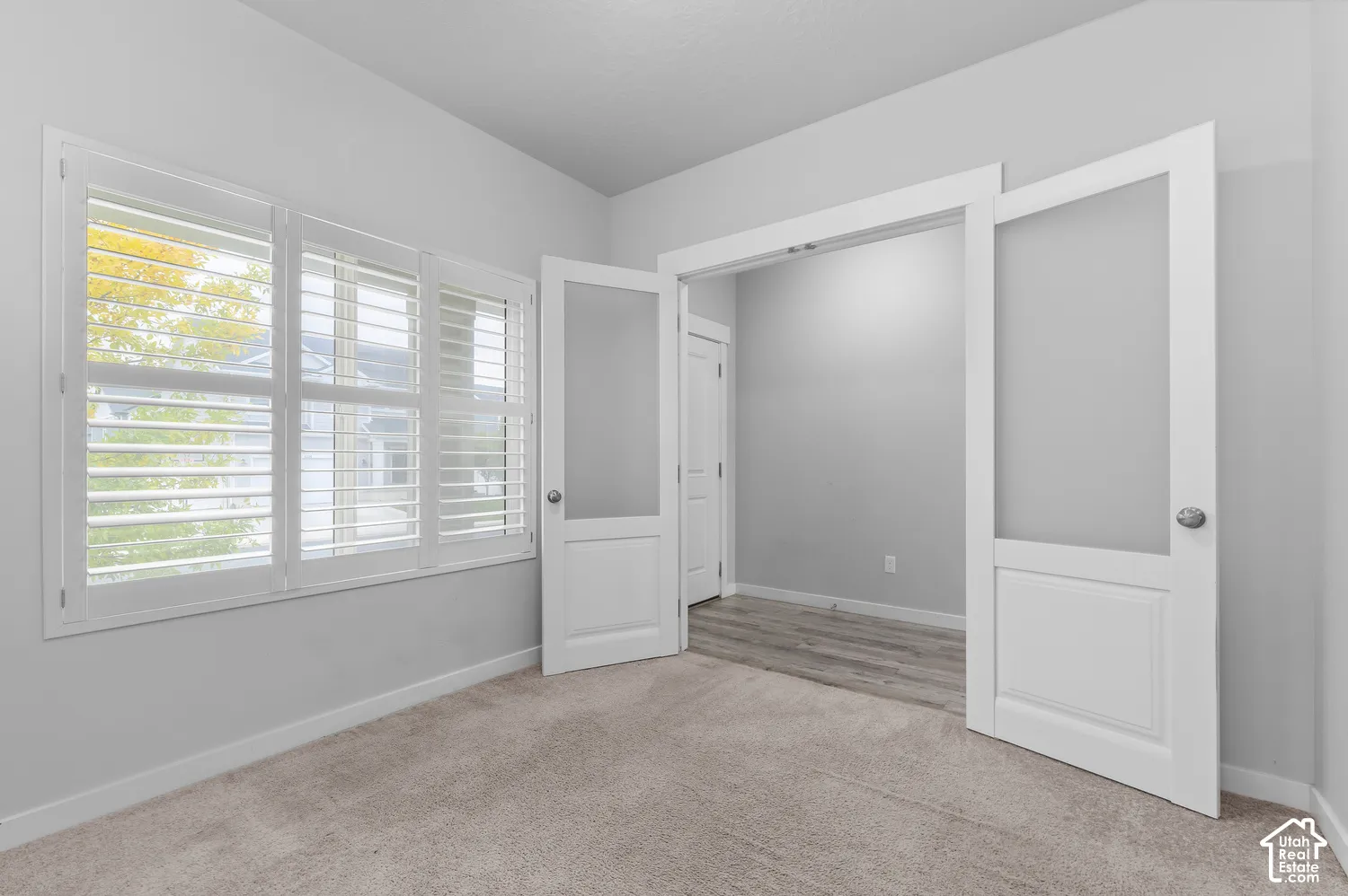 Interior space featuring white-trimmed glass-paneled double doors, interior plantation shutters, neutral-toned wall-to-wall carpeting, and wood-finish flooring