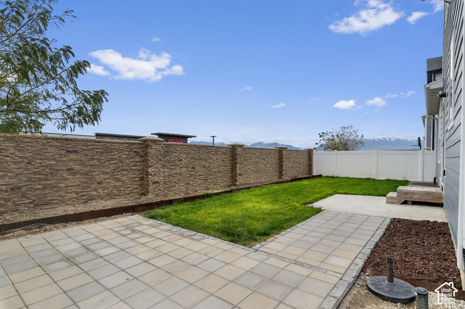 Rear yard featuring a stone-veneer perimeter wall, paved stone patio, maintained lawn, and mountain backdrop