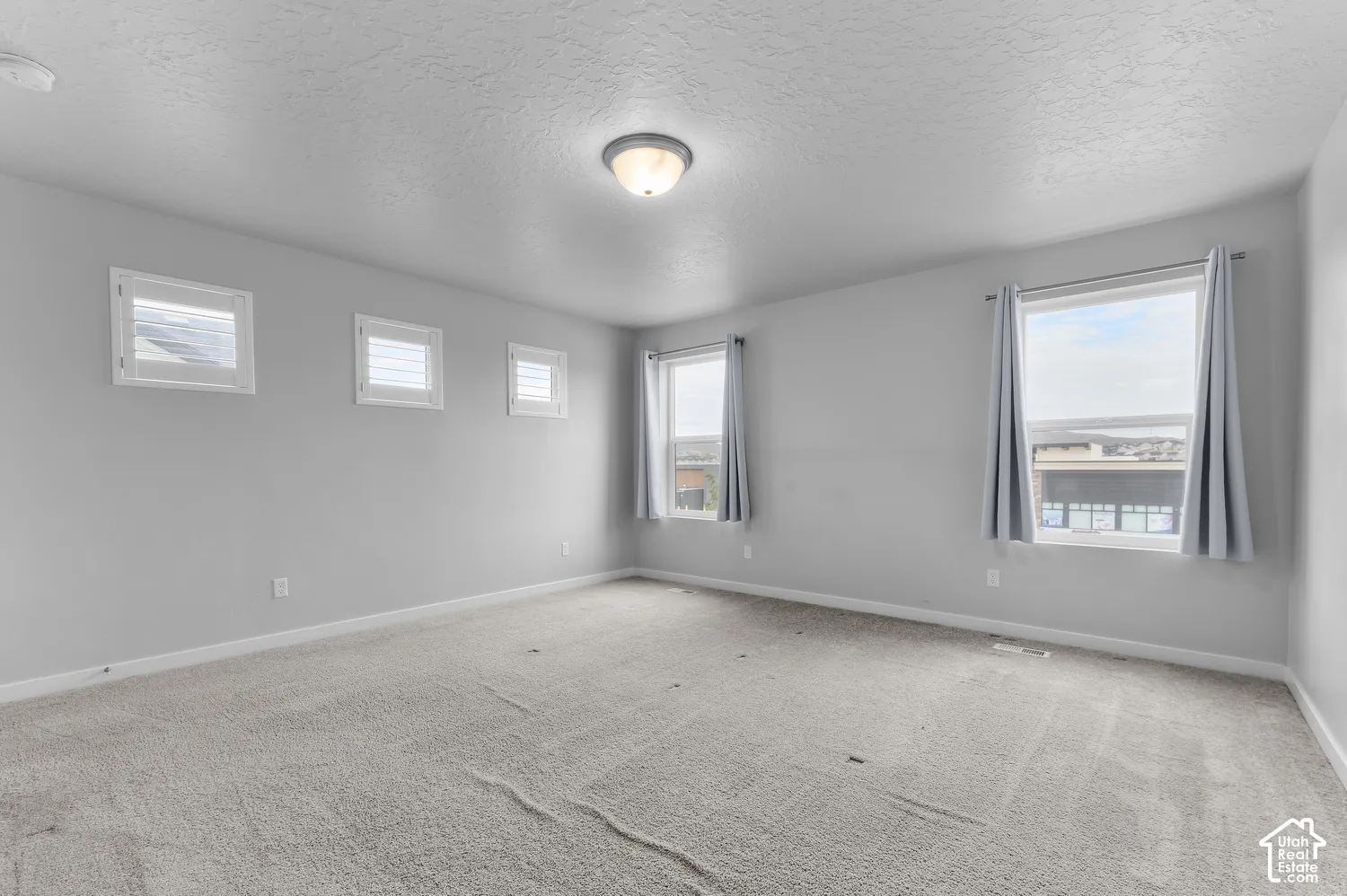 Room featuring neutral-toned carpeting, five windows with various sizes, and a centrally mounted dome-style light fixture