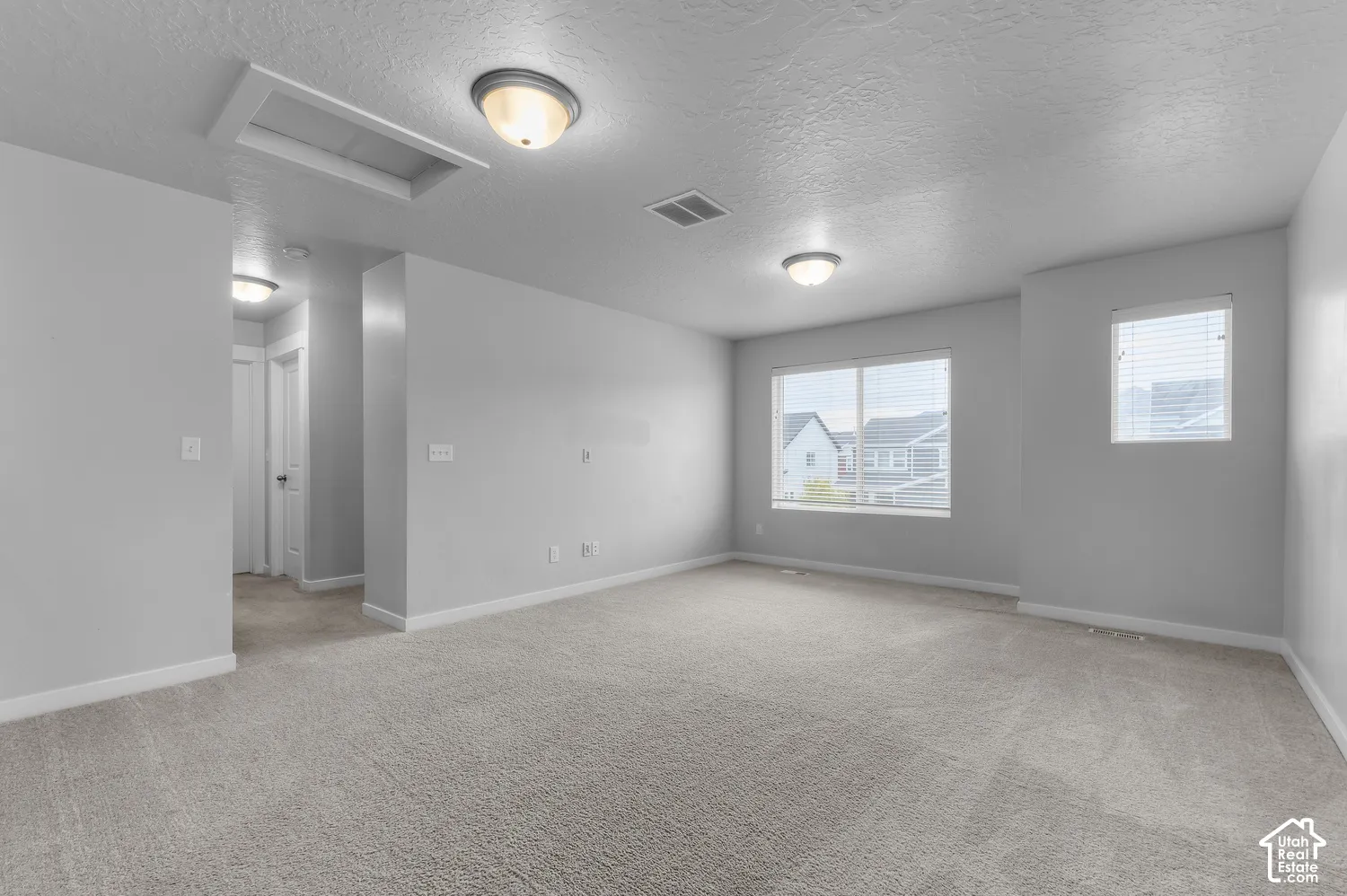 Neutral-toned interior space featuring wall-to-wall carpeting, multiple flush-mount light fixtures, and dual windows