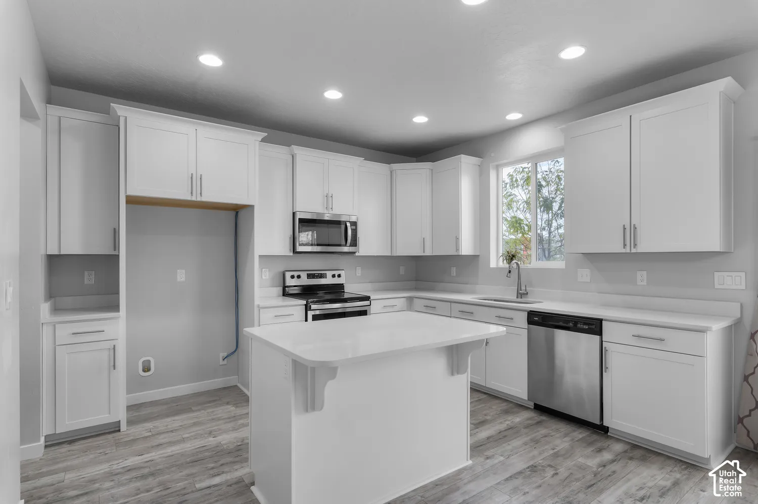 Kitchen featuring white shaker-style cabinetry, a central island with a solid-surface countertop, stainless steel appliances, recessed lighting, and wood-finish flooring